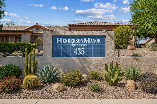 A sign for Henderson Manor Apartments is displayed in front of a building.