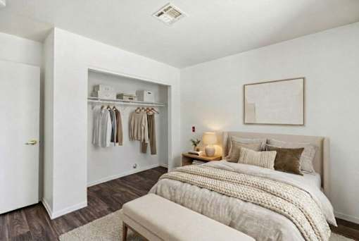 A bedroom with a bed, a bench, and a closet with clothes.