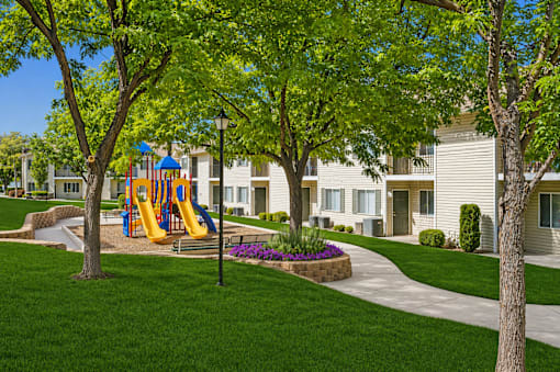A playground with a yellow slide is surrounded by green trees and a grassy area.