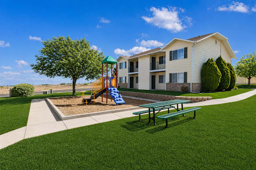 A playground with a slide and a bench is in front of a two-story building.