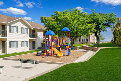 A playground with a slide and a swing set in front of apartment buildings.