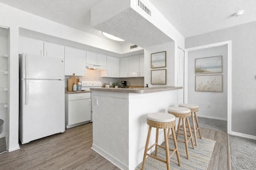 A kitchen with white appliances and a bar area with stools.
