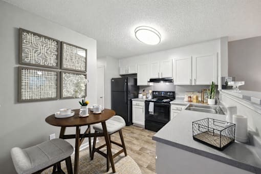 A kitchen with a table and chairs in the foreground and a refrigerator, oven, and sink in the background.
