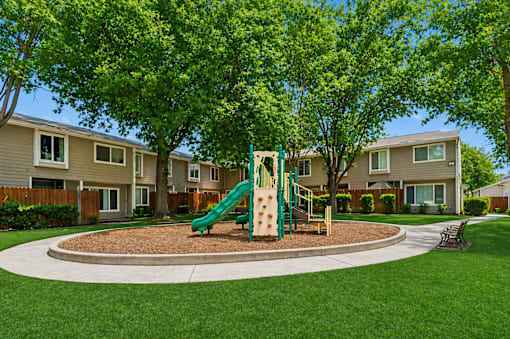 A playground with a green slide and brown sandbox in the middle of a grassy area.
