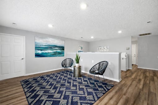 A room with a blue rug and a painting of a beach scene on the wall.