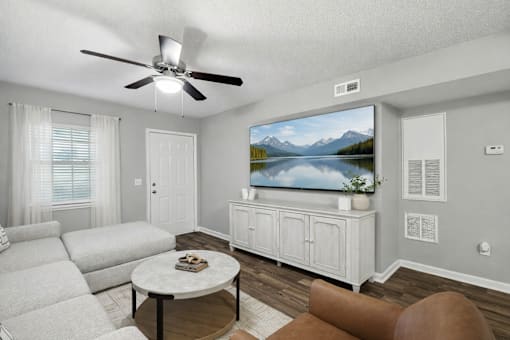 A living room with a white couch, a coffee table, and a television displaying a mountain landscape.