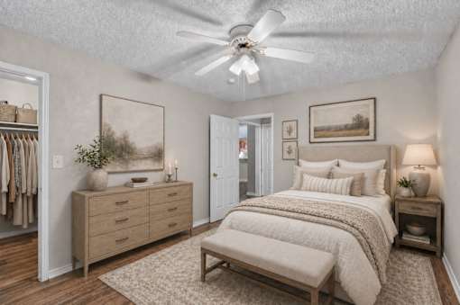 A bedroom with a bed, nightstand, and a dresser with clothes hanging on it.