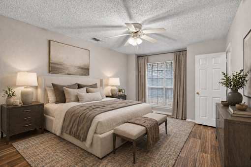A bedroom with a large bed, a ceiling fan, and a painting on the wall.