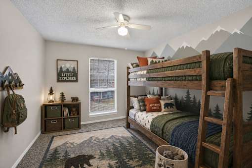 A room with a bunk bed, a rug with a bear on it, and a wall hanging that says "Little Explorer".