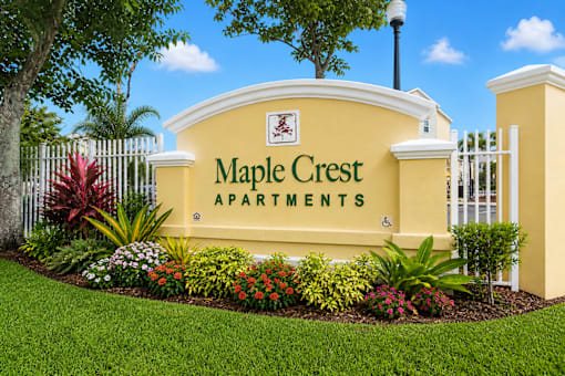 A sign for Maple Crest Apartments is displayed in front of a white fence.