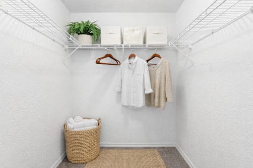 A white closet with clothes hanging and a basket on the floor.