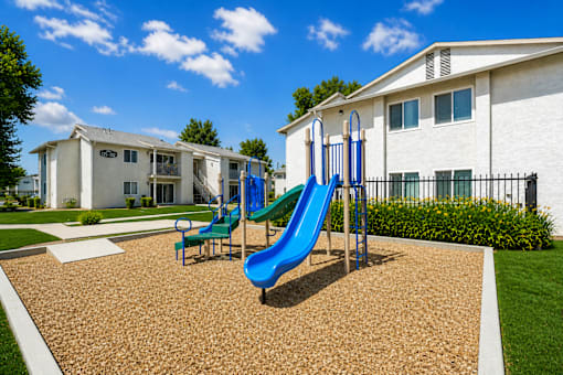 A playground with a blue slide and two chairs.