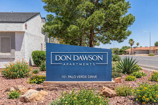A blue sign that says "Don Dawson Apartments" in front of a building.