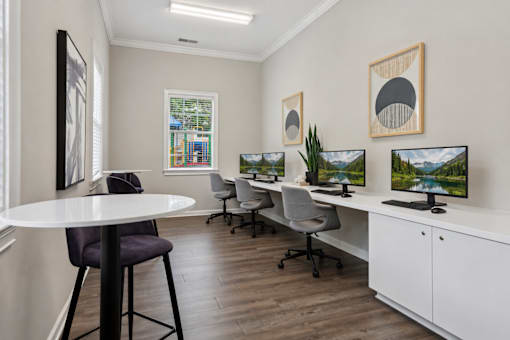 A room with a white table and chairs, a white desk with a computer, and two framed pictures on the wall.