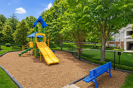 A playground with a yellow slide and a blue bench.