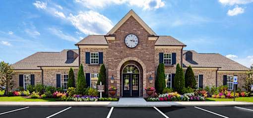 A brick building with a clock on the front and a parking lot in front.