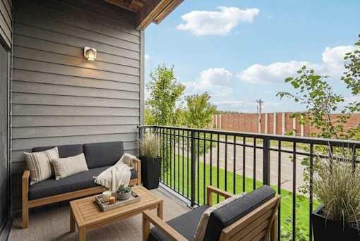 A cozy balcony with a sofa, chair, and potted plants.