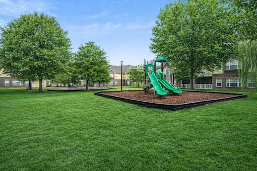 A playground with a green slide in the middle of a grassy area.