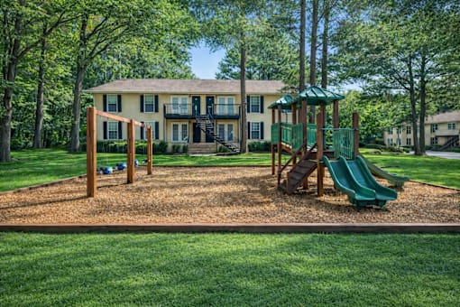 A playground with a green slide and a wooden swing set in front of a two-story house.