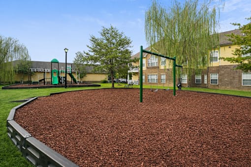 A playground with a red surface and a green swing set.