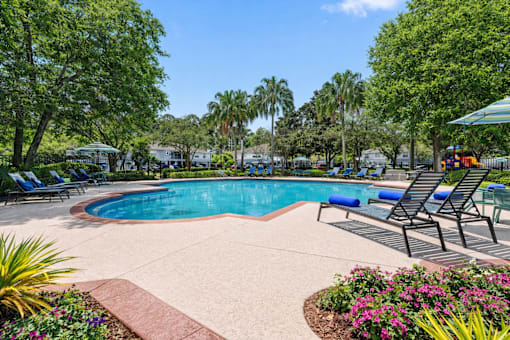 A pool surrounded by trees and chairs.