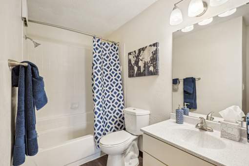 A white bathroom with a blue towel hanging on the shower rod.