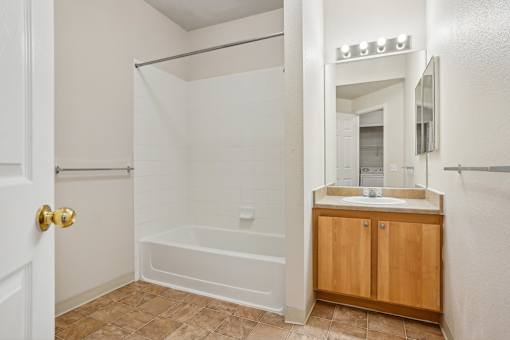 A white bathroom with a wooden cabinet and a white tub.