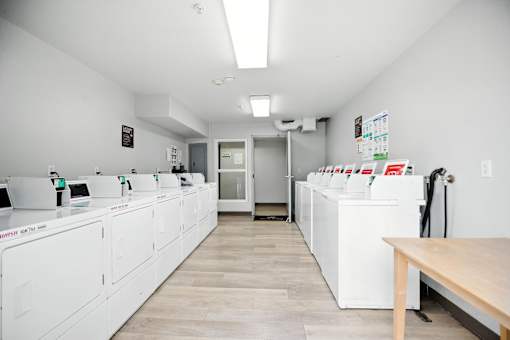 A clean, white-walled room with a row of white appliances and a wooden table.