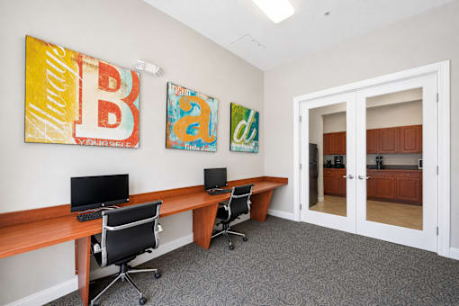 A room with a desk, chairs and two paintings on the wall.
