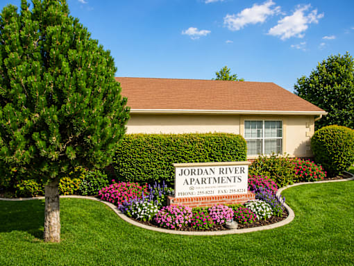 A well-maintained lawn surrounds a building with a sign that reads "Jordan River Apartments.".