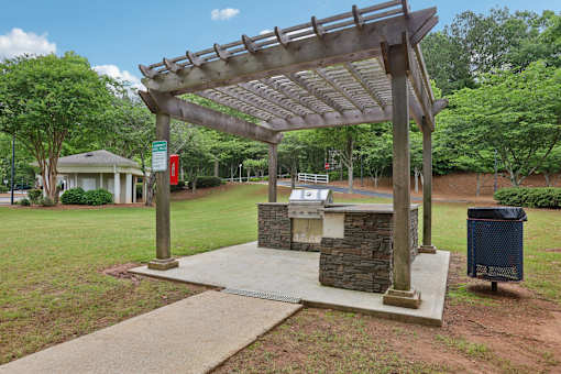 A wooden pergola is over a stone and concrete fireplace.