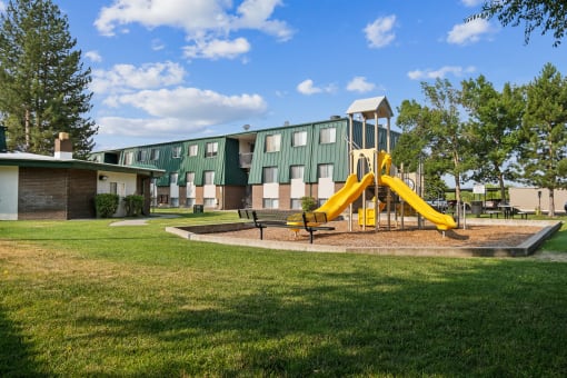 a playground with a yellow swing set in front of a building
