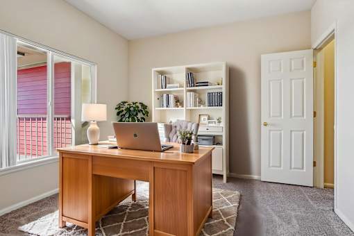 A room with a desk, laptop, and bookshelf.