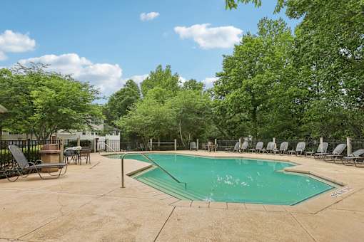A pool surrounded by trees and chairs.