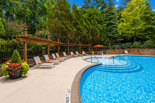 A pool surrounded by trees and chairs.