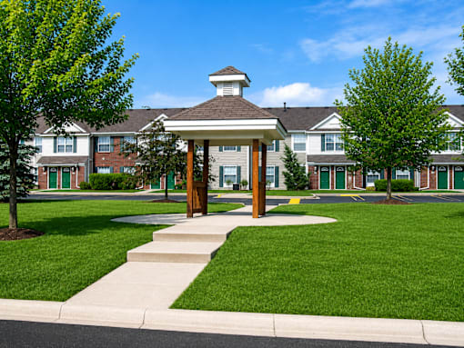 A gazebo-like structure sits in the middle of a grassy area in front of apartment buildings.