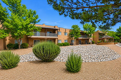 A building with a brown facade surrounded by greenery and a gravel area.