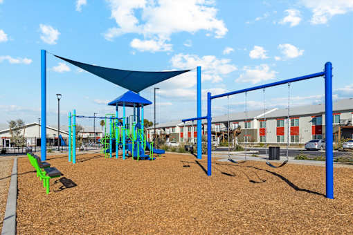 A playground with a blue shade structure and a swing set.