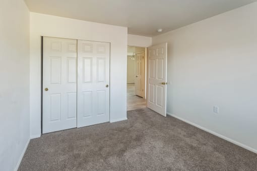 a bedroom with white doors and carpeting and a door to a hallway