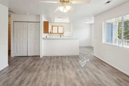 an empty living room with a kitchen and a ceiling fan