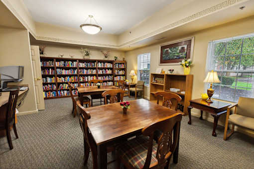 A room with a long table surrounded by chairs and a bookshelf filled with books.