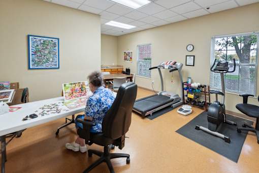A woman in a blue shirt is sitting at a table in a room with exercise equipment.
