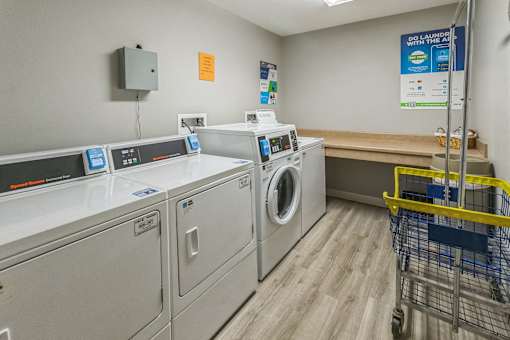 A laundromat with washers and dryers and a shopping cart.