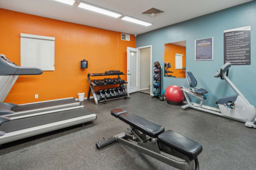 A gym with orange walls has a treadmill, weights, and a bench at Vista Linda, Santa Fe, 87507