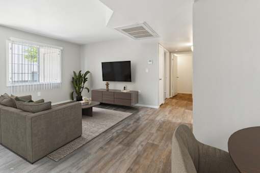 A living room with a grey couch, a brown armchair, a wooden floor, and a flat-screen TV mounted on the wall.
