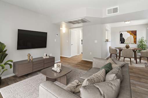 A living room with a grey couch, a coffee table, and a flat screen TV mounted on the wall.