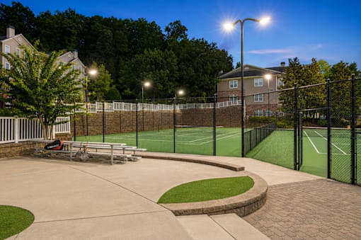 A tennis court surrounded by a black fence with a bench and a lamp post.