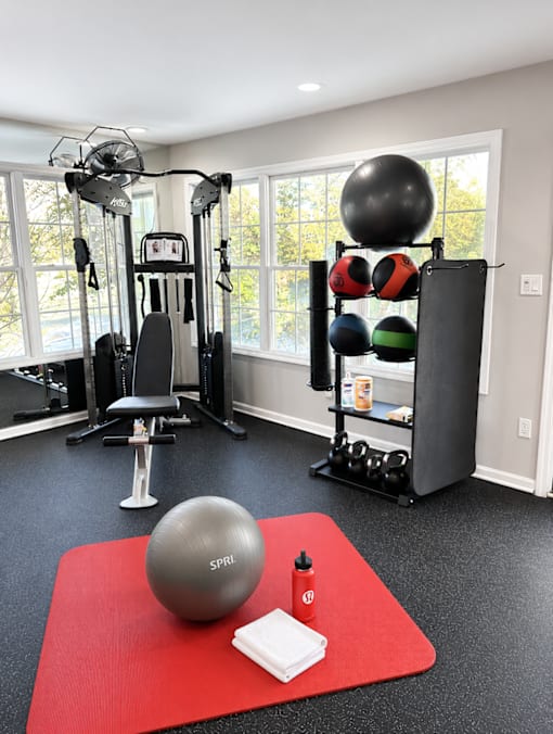 A gym room with a variety of equipment including a weight rack, a bench, and a ball.