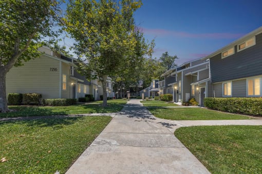 a walkway between houses with trees and grass