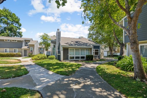 a walkway between two houses with trees and grass